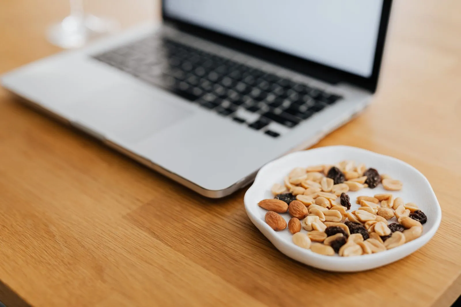 A plate of mixed nuts beside a laptop on a wooden desk, perfect for remote work inspiration.